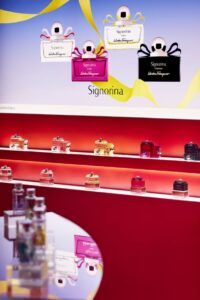 Luxury fragrance display featuring illuminated faux marble shelves and Signorina perfume bottles in a vibrant seasonal retail setup.