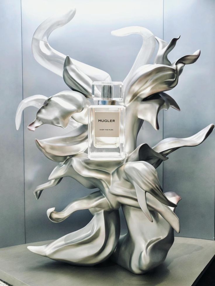 Artistic metal display stand with fluid, sculptural curves supporting a luxury perfume bottle, blending high-end design innovation with modern retail presentation.