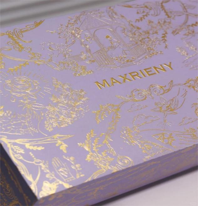 Luxury packaging box with gold foil stamping details and intricate decorative patterns on a purple surface