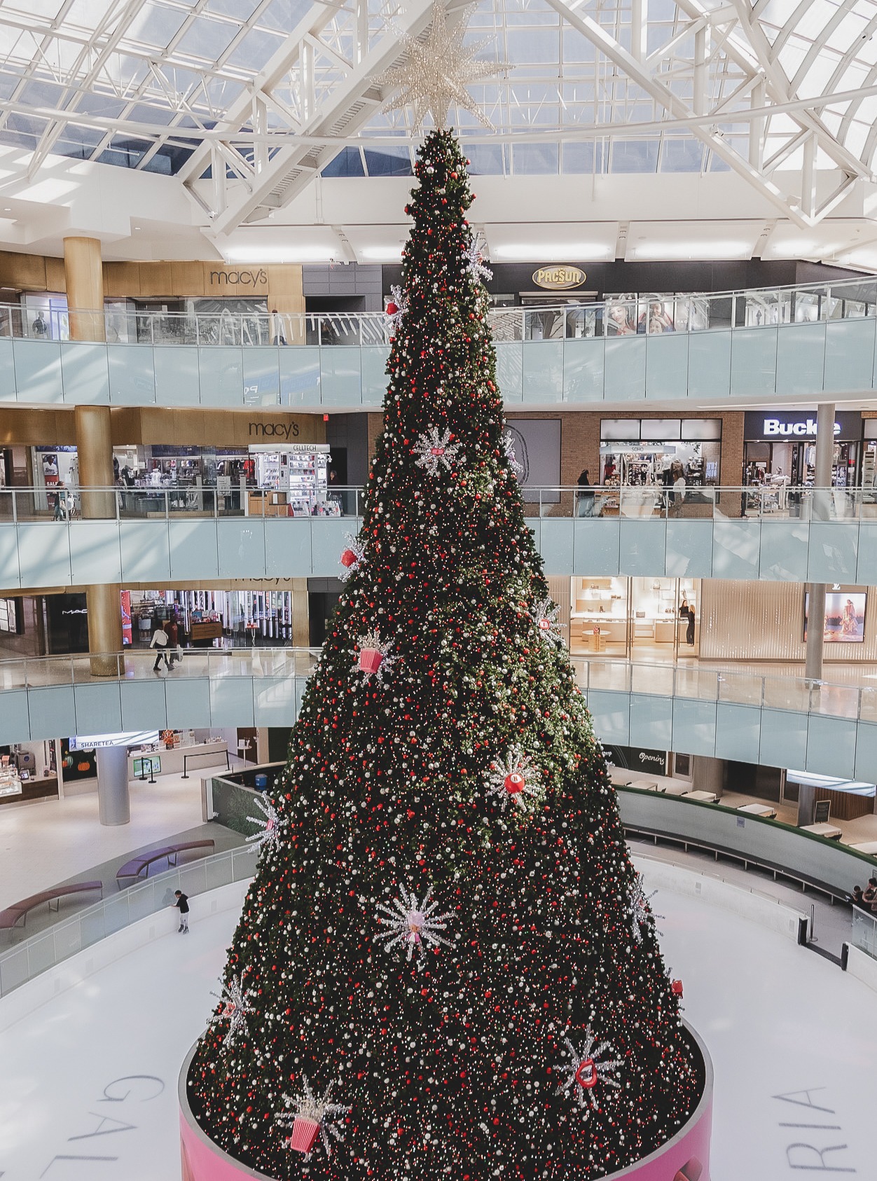 Giant mall Christmas tree viewed from upper floor, showing scale, hanging ornaments, and retail environment constraints.
