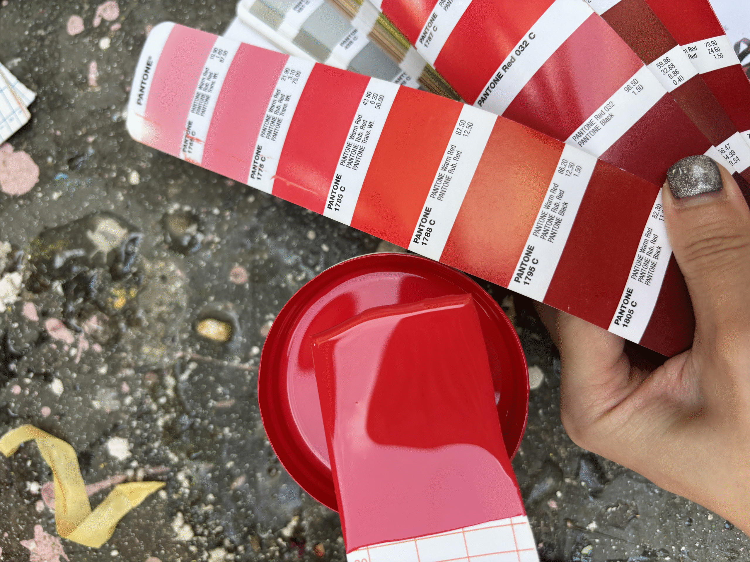 Paint team cross-referencing Netflix red paint sample against Pantone color book during production, testing across multiple prop materials before full production run