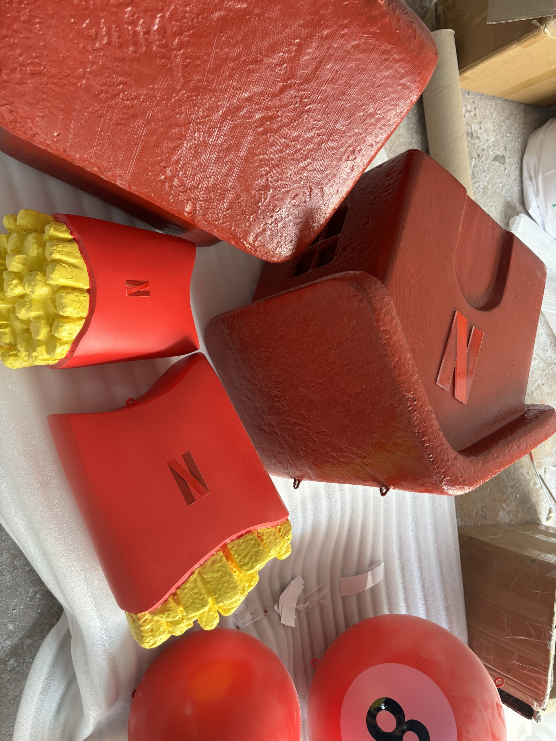 Painted red house props and oversized French fries props placed on the workshop floor for final quality control before packing.