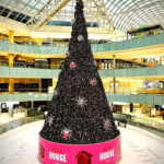 A 95-foot Christmas tree installation inside Galleria Dallas for Netflix House, featuring oversized holiday decorations and custom retail display elements produced for a large shopping mall Christmas installation.