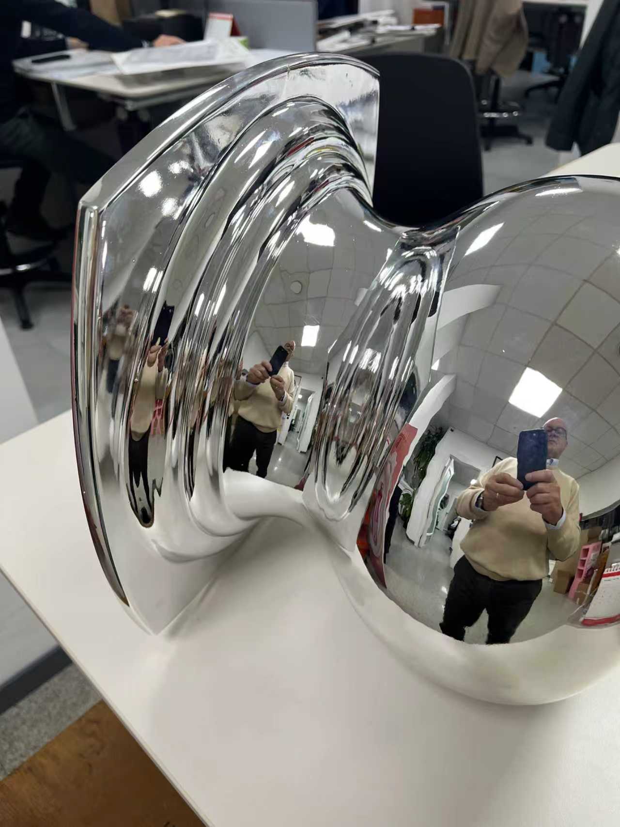 A close up side angle shot of a shiny chrome perfume bottle cap sample revealing flawless surface consistency and sharp curvature lines under directional office lighting.