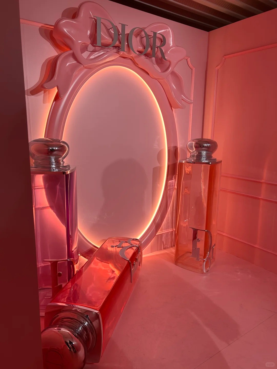 Front view of oversized clear pink fragrance bottle replicas arranged in a monochromatic pink room decoration in front of a giant decorative mirror.