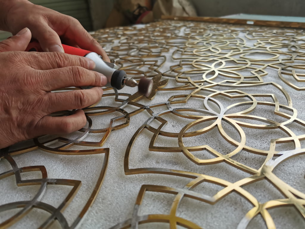 Craftsman using a rotary tool to finish the edges of an intricate floral metal panel