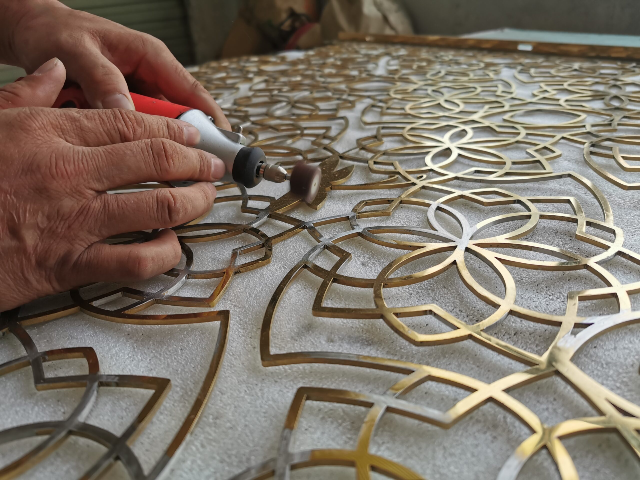 Craftsman using a rotary tool to finish the edges of an intricate floral metal panel