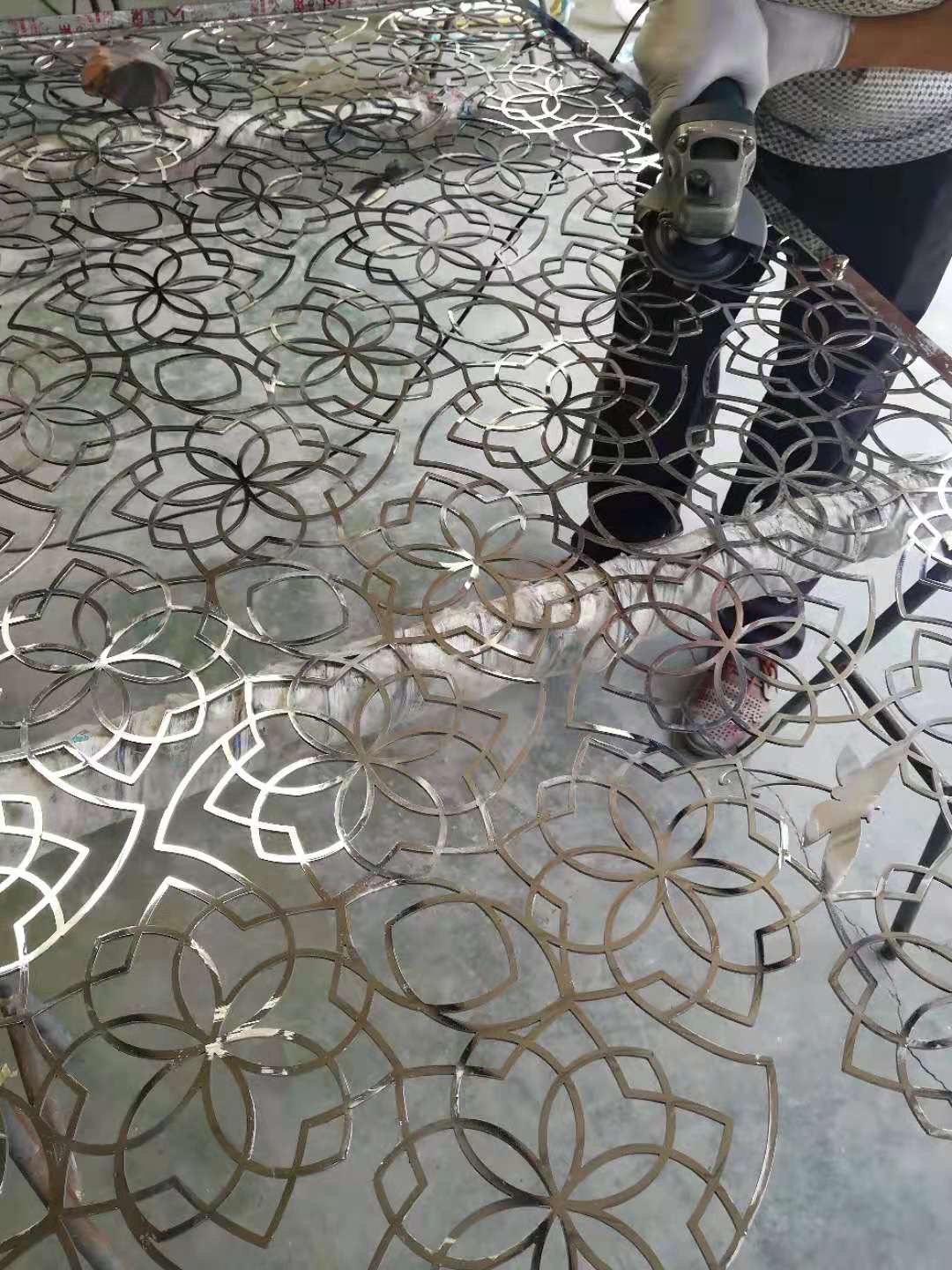 Worker grinding a large decorative metal panel with repeating floral cutout patterns