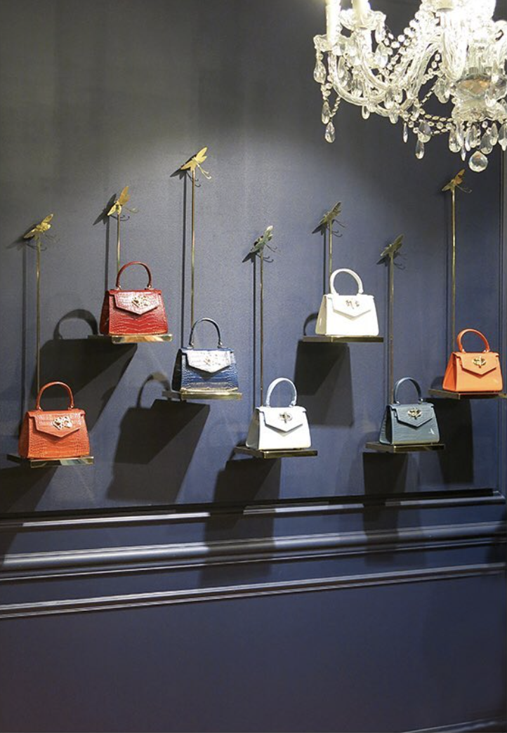 Luxury handbag display with slim metal supports and decorative dragonfly elements at different heights