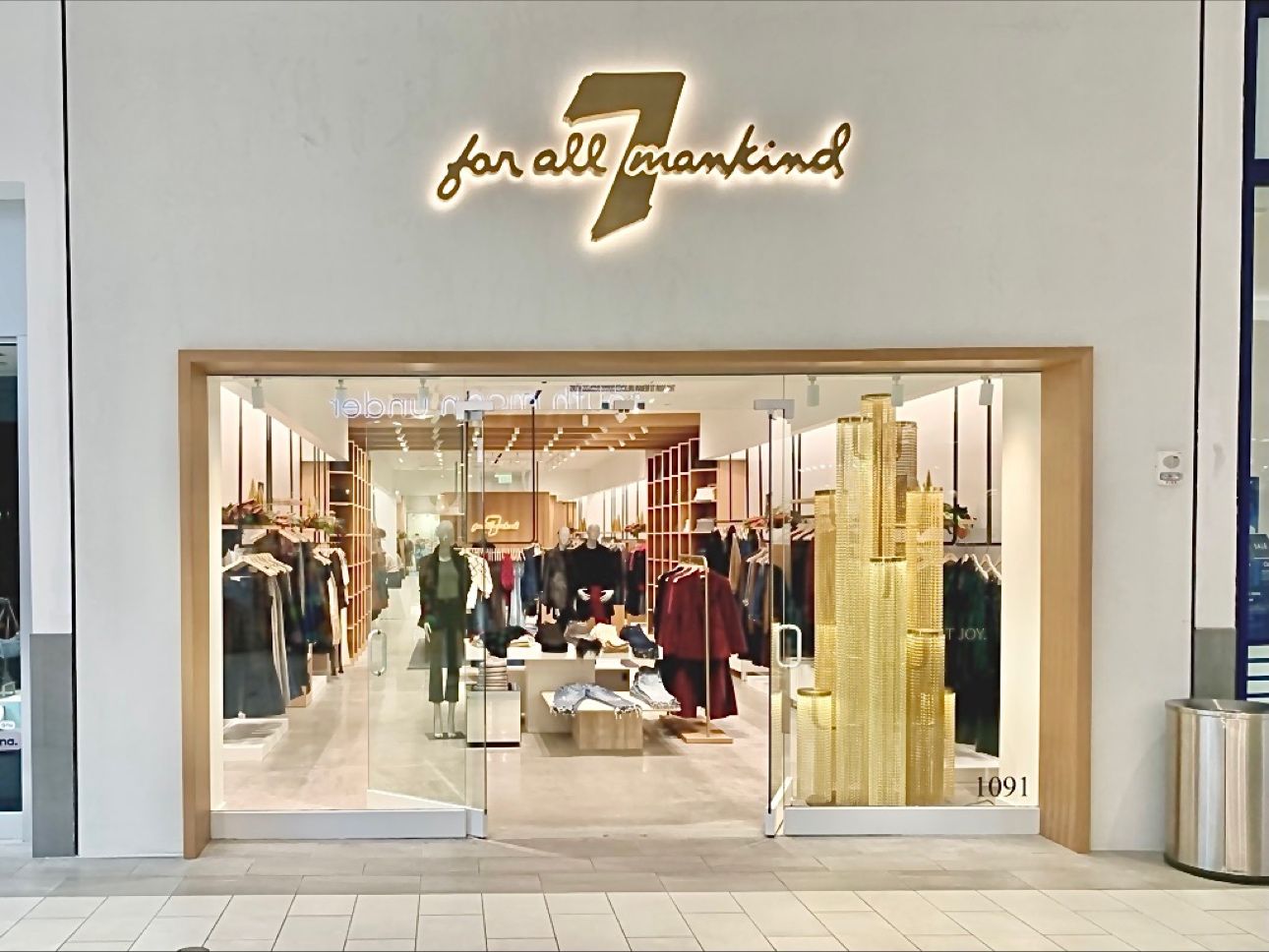 Christmas tree prop with illuminated gold chain columns installed at a fashion retail storefront.