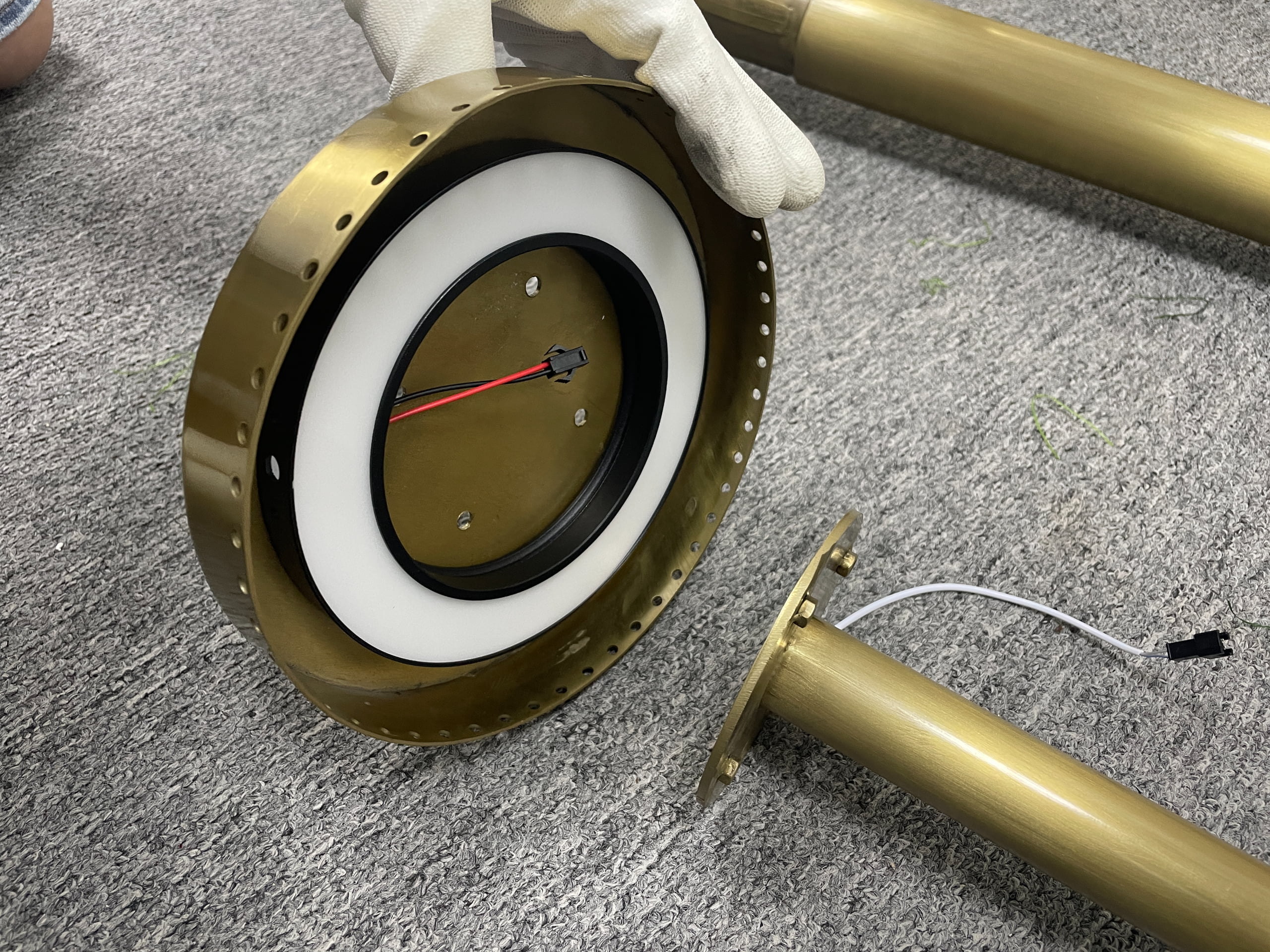 Close-up of a circular LED ring module connected to a brushed gold metal branch with a detachable electrical connector.