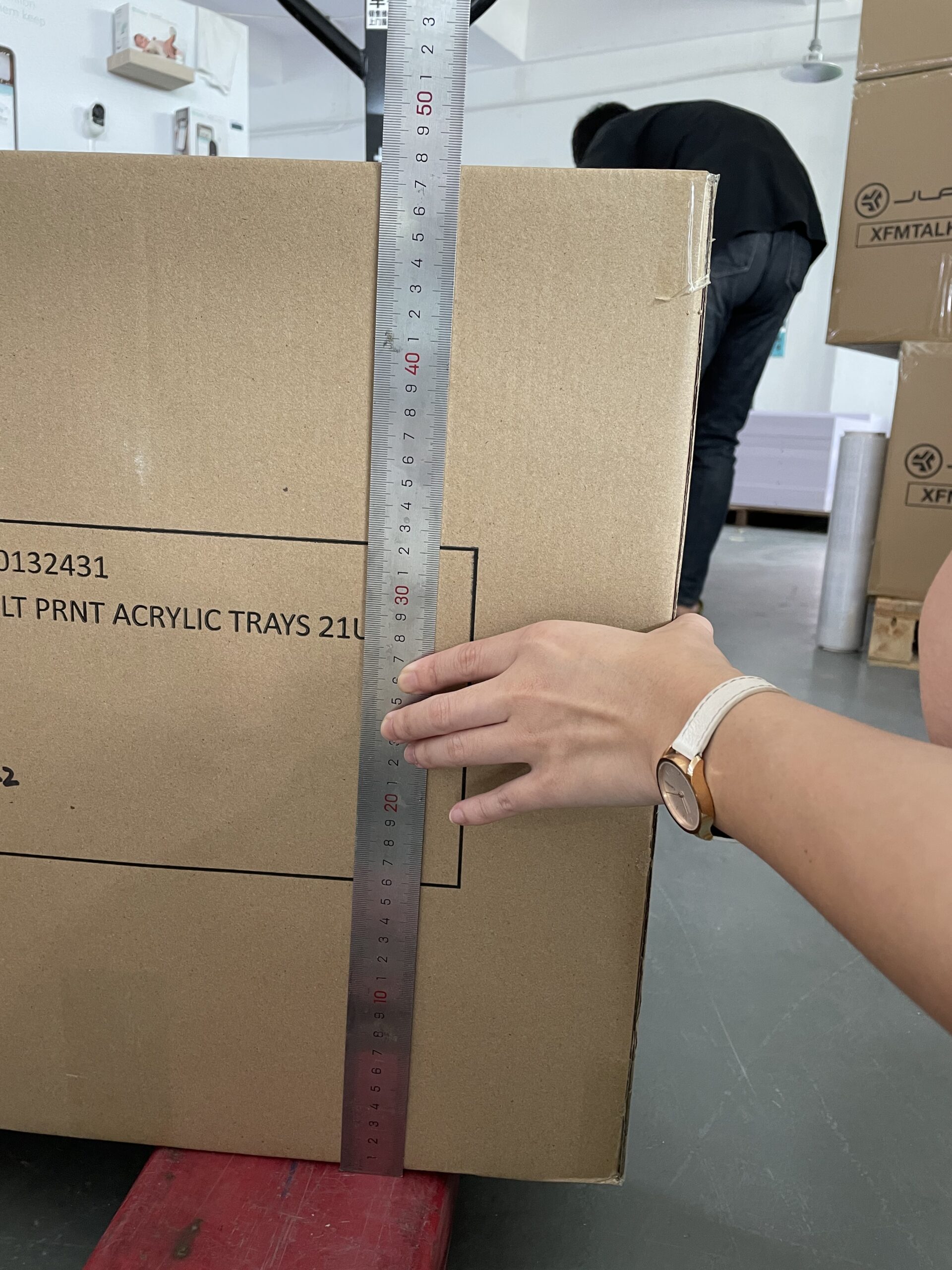 Factory worker checking outer carton dimensions with a metal ruler before shipment