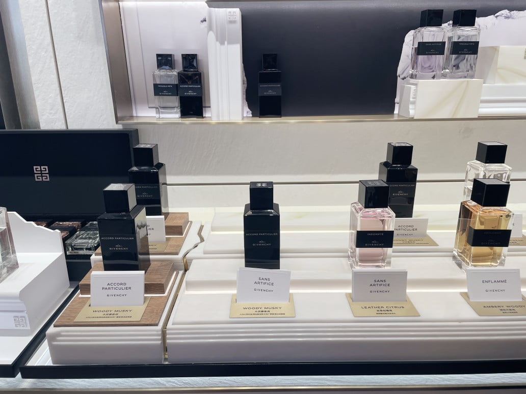 Perfume retail display prototype showing acrylic components positioned near fragrance tester bottles -- checking material suitability for potential chemical contact